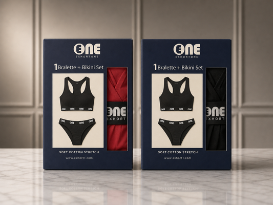 Two navy blue retail boxes for ONE Exportone bralette and bikini sets standing on a light marble surface against a paneled wall. The left box shows a black bralette and bikini set with a red bikini bottom visible through the window, and the right box shows a black bikini set with a black bikini bottom visible through the window.