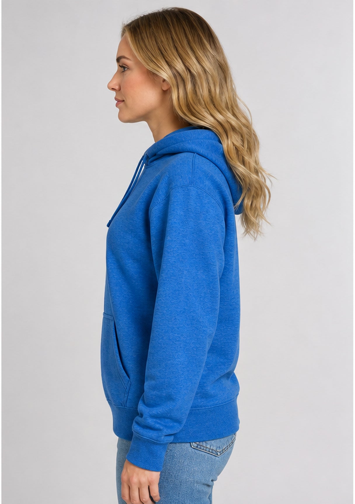 A woman in profile wearing a heather blue pullover hoodie and light blue jeans, photographed against a plain light gray studio background.
