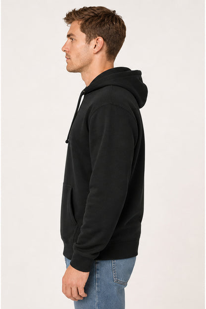 A man in profile wearing a black pullover hoodie and blue jeans, standing against a plain light background.