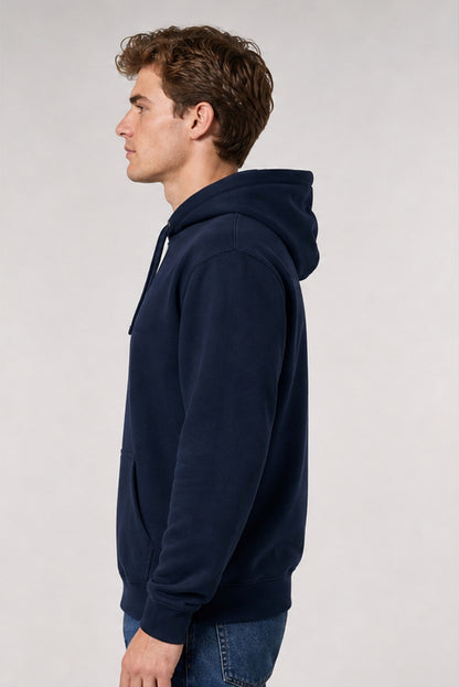 A man in profile wearing a navy blue pullover hoodie and blue jeans, photographed against a plain light gray studio background.