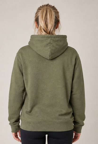 A woman viewed from the back wearing an olive green pullover hoodie and black pants, standing against a plain light beige studio background.