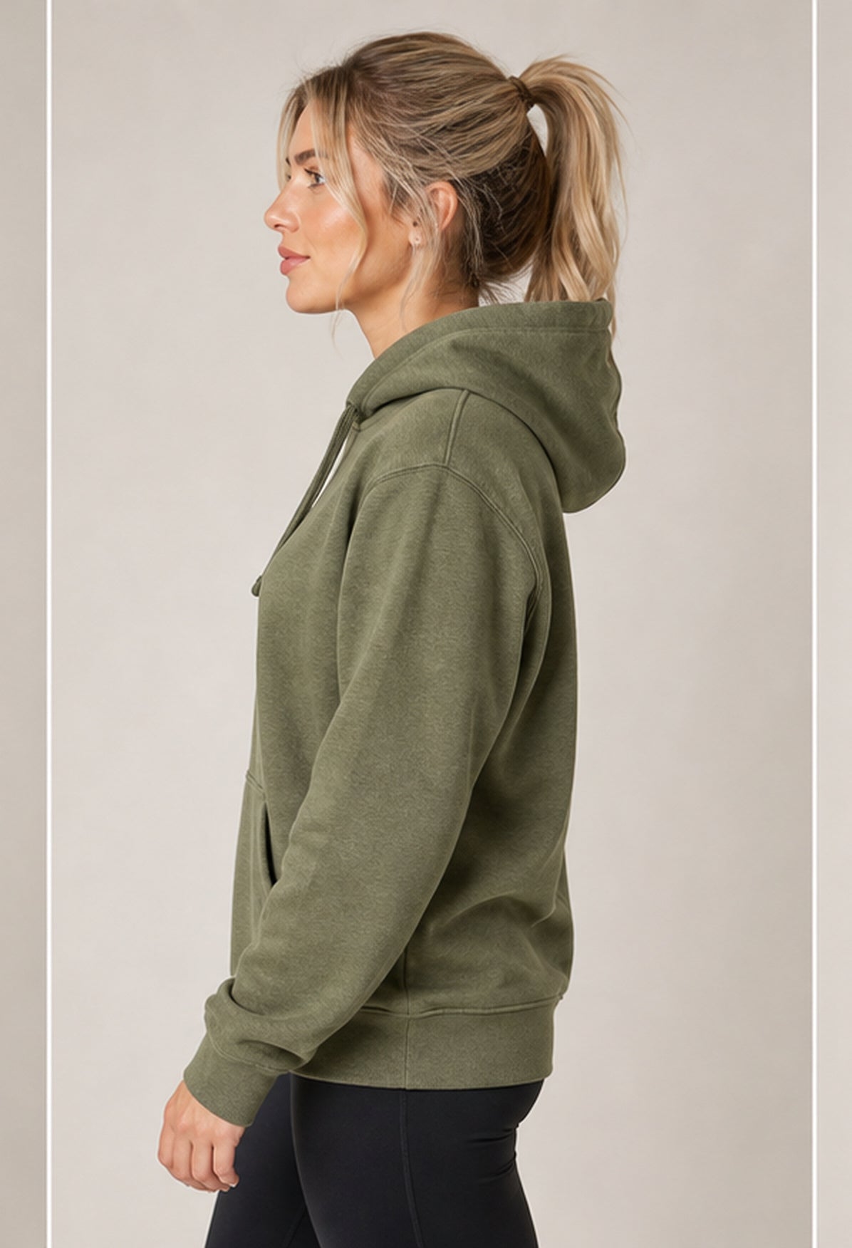 A woman in profile wearing an olive green pullover hoodie and black leggings, standing against a plain light gray studio background.