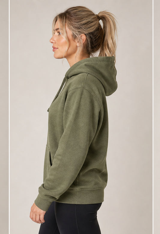 A woman in profile wearing an olive green pullover hoodie and black leggings, standing against a plain light gray studio background.