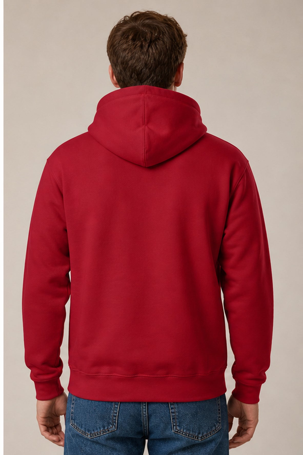 A man viewed from behind wearing a solid red pullover hoodie and blue jeans, standing against a plain beige studio background.