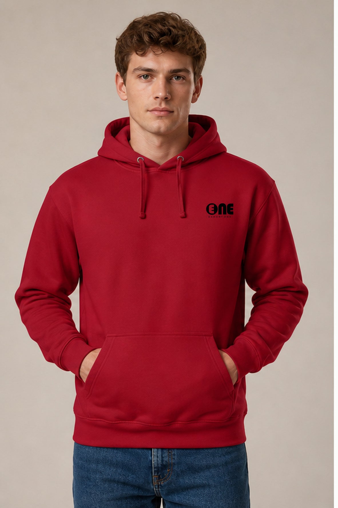 A man wearing a red pullover hoodie with a black 'ONE' logo on the left chest, paired with blue jeans, standing against a plain beige studio background.