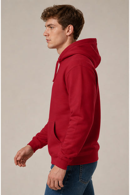 A man in profile wearing a solid red pullover hoodie and blue jeans, standing against a plain light beige studio background.