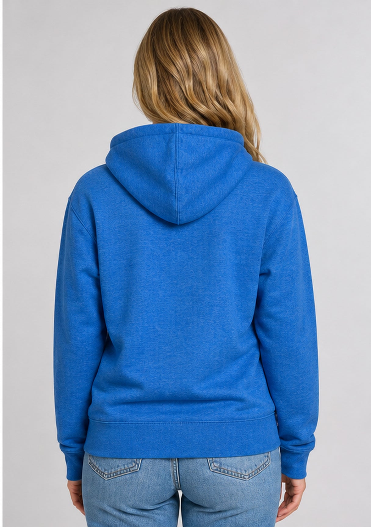 A woman viewed from the back wearing a heather blue pullover hoodie and light blue jeans against a plain light gray studio background.